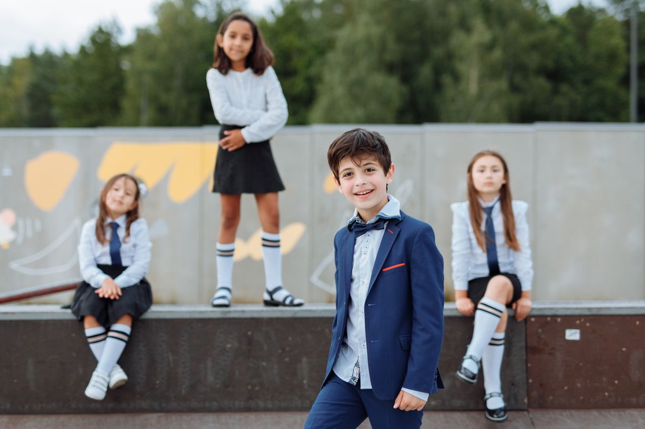 Diverse children in school uniforms smiling and posing outdoors on a sunny day.